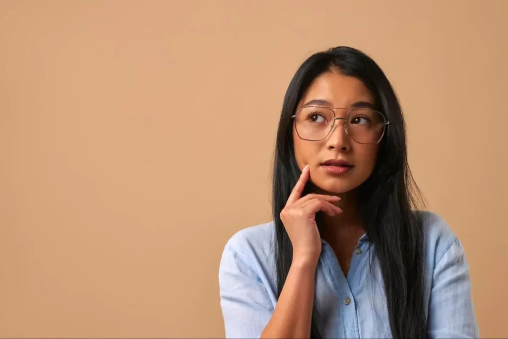 Young Asian woman with glasses looking upward thoughtfully, representing someone seeking clarity through a Bazi consultation in Singapore