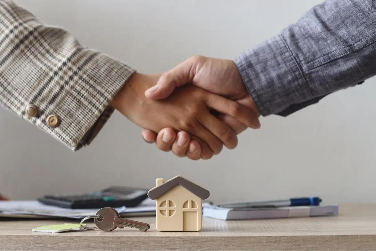 Agreement on a house purchase Two people shaking hands beside a model house and keys